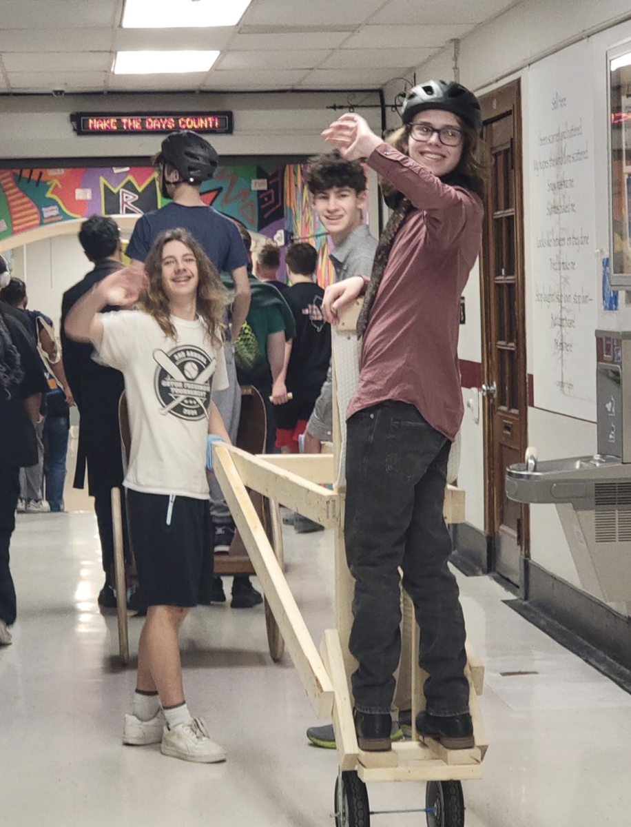 Desmond McCue, Oliver Crumrine, and Jackson Harker march down the hallway of Ridgewood High School on their homemade chariot.